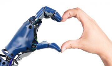 Hands creating a heart shaped; one human hand and one robot hand.
