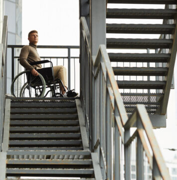 A young man in a wheelchair looking down at inaccessible outdoor stairs