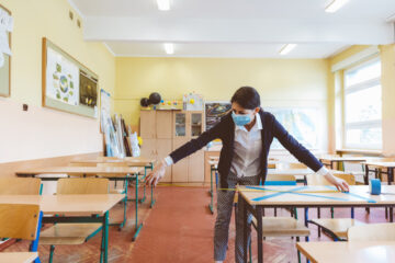 COVID19 Pandemic - A teacher wearing a facemask measures the distance between desks in a classroom. 