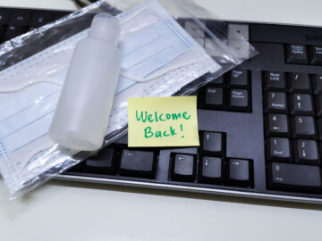 (alt="keyboard with COVID prevention items, a face mask and hand sanitizer. With a welcome back note")