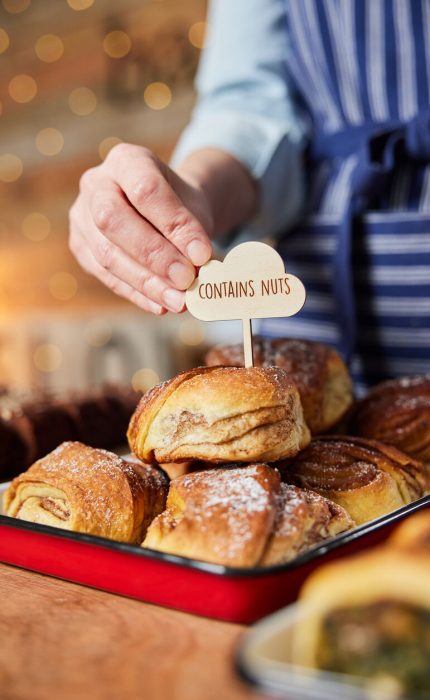 (alt=" person placing a sign "contains nuts" onto baked goods")